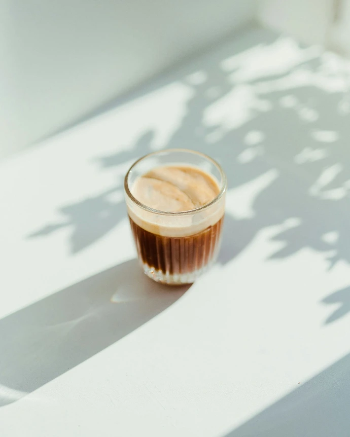 clear drinking glass with coffee on top of white table